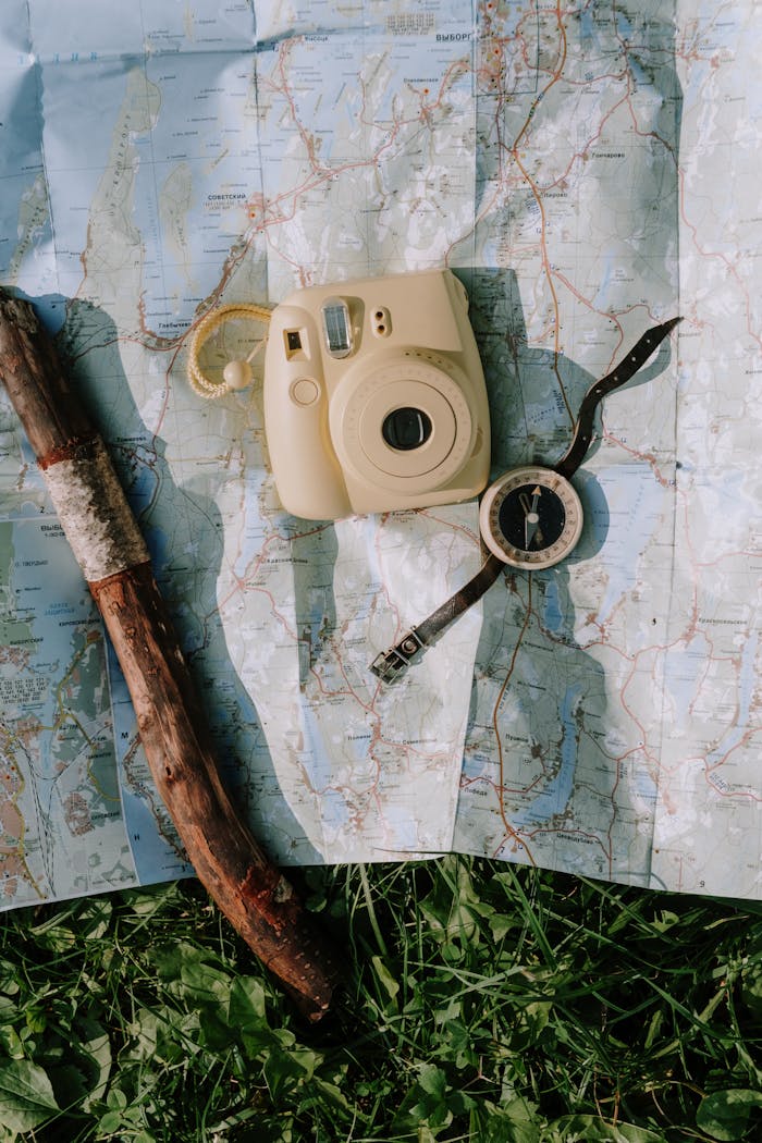Flat lay of vintage camera, compass, and walking stick on a map outdoors. Perfect for travel and adventure themes.
